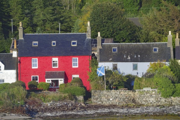 Red house with Scottish flag surrounded by trees and a stone wall in a seaside village, Dornie, Highlands, Scotland, United Kingdom