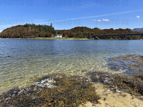 View over a loch with bridge and house surrounded by wooded hills under a blue sky, Silver Sands of Morar, Morar, film set, Scotland, United Kingdom
