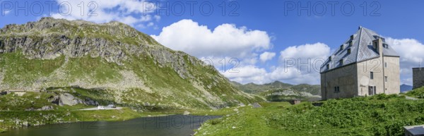 Panoramic photo view to the right left side of Ospizio Hospiz Herberge San Gottardo St. Gotthard built in the 13th century from 1230 with small entrance door main entrance to chapel Cappella di San Gottardo on pass summit of Gotthard Pass, left mountain lake Lago di Monti, Swiss Alps, Airolo, Canton Ticino, Ticino, Switzerland