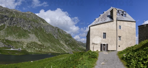 View to the right left side of the building of Ospizio Hospiz Herberge San Gottardo St. Gotthard built from 1230 in the 13th century with small entrance door main entrance to chapel Cappella di San Gottardo on top of Gotthard pass, left mountain lake Lago di Monti, Swiss Alps, Airolo, Canton Ticino, Ticino, Switzerland