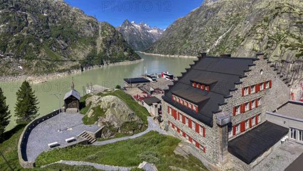 View from an elevated position to the right of the Grimselhospiz Hotel, built in 1932 on the Nollen, the first electrically heated hotel in Europe, on the left the Grimsel Hospiz mountain chapel, in the background Grimselsee, Guttanen, Canton of Bern, Switzerland