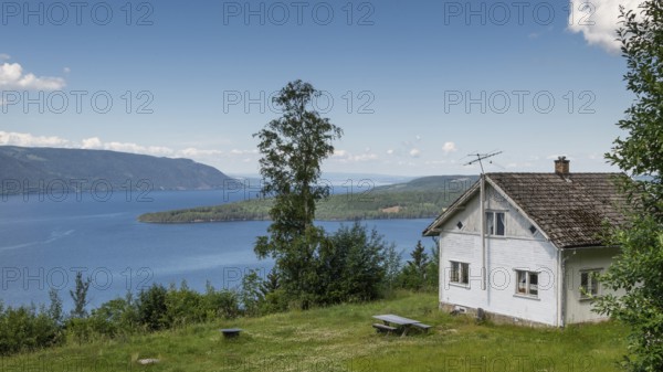 White house in a meadow, view opens onto Lake Mjøsa or Mjosa and forested mountain ridges, Olavsweg or Olavsleden, near Tangen, Norway