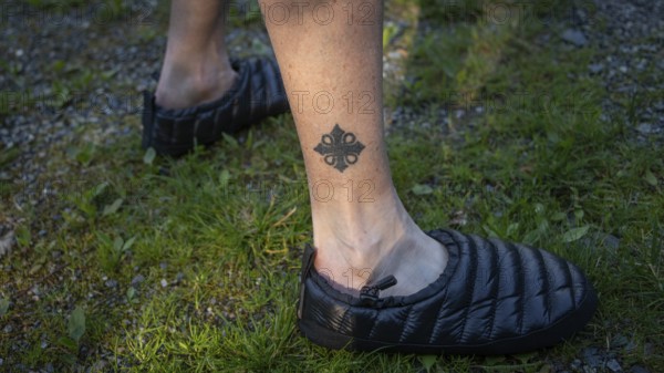Leg tattooed with Olav's cross, pilgrim in tap shoes on grassy ground, Olavsweg or Olavsleden, Norway