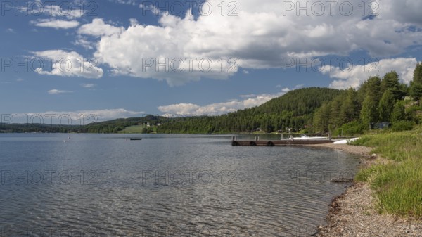 View of bathing area at Lake Mjøsa or Lake Mjosa with wooded shore under blue sky, Olavsweg or Olavsleden, near Tangen, Norway