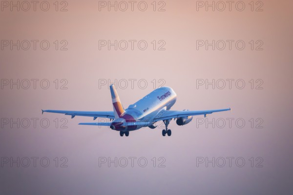 A Eurowings aeroplane takes off and disappears into an orange evening sky, Stuttgart, Baden-Württembwerg, Germany