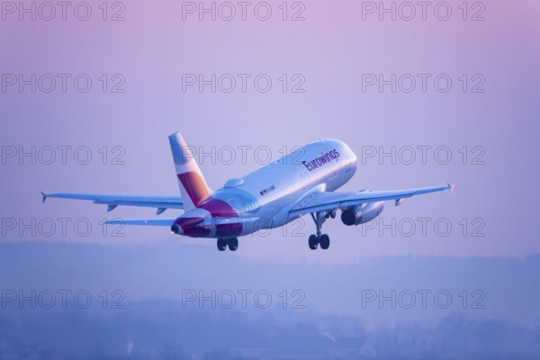 A Eurowings aircraft soars in a pink-coloured sky, Stuttgart, Baden-Württembwerg, Germany