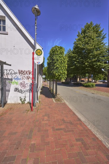 Bus stop church of the lines 670 Rieste and 672 Thiene, building, graffiti, lantern, trees, blue sky, cirrostratus clouds, main street, Alfhausen, district Osnabrück, Lower Saxony, Germany
