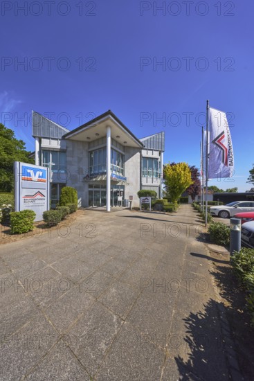 Vereinigte Volksbank eG - Filiale Alfhausen, Baugenossenschaft Landkreis Osnabrück eG, flags on flagpoles, modern architecture, street, car park with vehicles, flower bed, trees, hedge, blue sky, cirrostratus clouds, Hauptstraße, Alfhausen, Landkreis Osnabrück, Lower Saxony, Germany