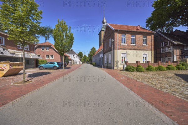 Street, church tower of St. Johannis, brick building, trees, blue sky, cirrostratus clouds, main street, Alfhausen, district of Osnabrück, Lower Saxony, Germany