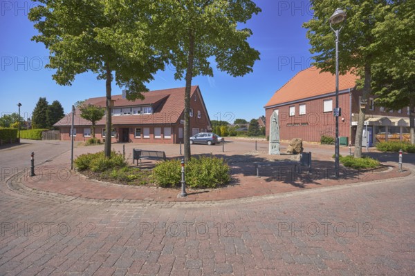 Roads, bollards, trees, bench, 1000 year fountain, shady, clinker pavement, concrete paving stone road, clinker building, lantern, hedges, blue sky, cloudless, intersection of Hauptstraße with Nonnenpfad and In den Gärten, Alfhausen, Osnabrück district, Lower Saxony, Germany