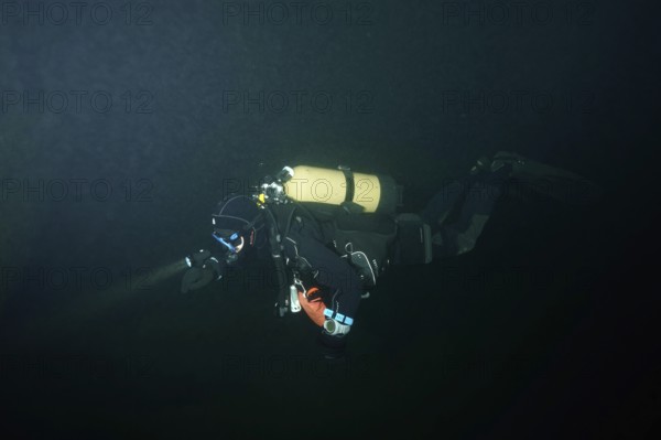 A diver in a diving suit explores a dark underwater environment. Dive site wreck of the Jura, Lake Constance, Bottighofen, Switzerland, Münsterlingen, Germany