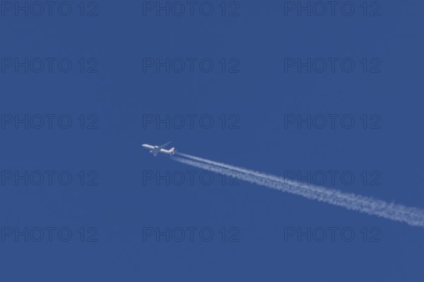 Jet passenger aircraft of American Airlines flying with vapour trails or contrails behind in a blue sky, England, United Kingdom