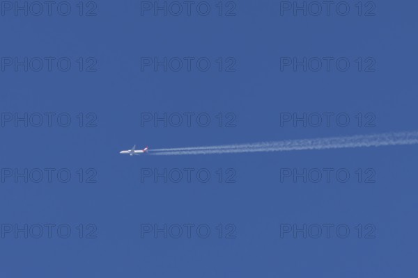 Jet passenger aircraft of Austrian Airways flying with vapour trails or contrails behind in a blue sky, England, United Kingdom