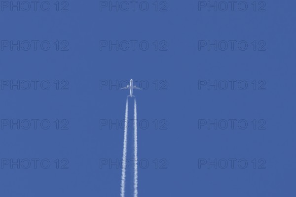 Jet passenger aircraft flying with vapour trails or contrails behind in a blue sky, England, United Kingdom