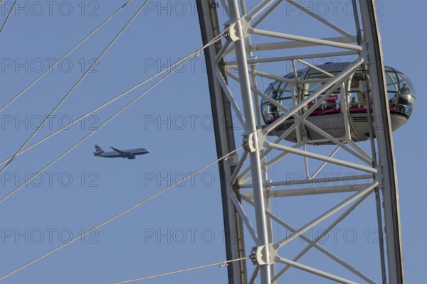 Airbus A320-232 jet passenger aircraft of British Airways airlines in flight in a blue sky with the London Eye wheel in the foreground, London, England, United Kingdom
