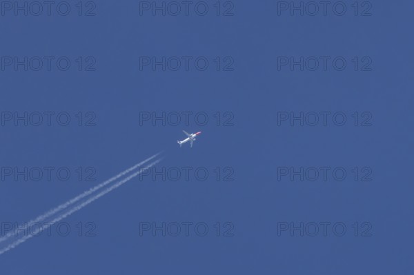 Boeing 737 jet passenger aircraft of Norweign Air with a vapour trial or contrail behind flying in a blue sky, England, United Kingdom
