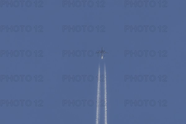 Jet passenger aircraft flying with vapour trails or contrails behind in a blue sky, England, United Kingdom