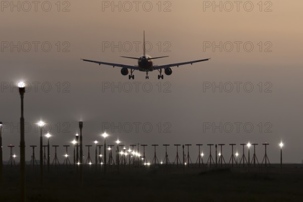 Airbus jet passenger aircraft in flight landing at sunset over runway lights at London Stansted airport, Essex, England, United Kingdom