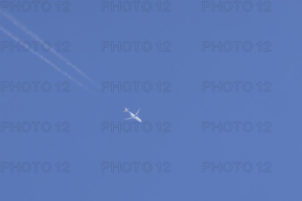 Jet passenger aircraft flying with vapour trails or contrails behind in a blue sky, England, United Kingdom