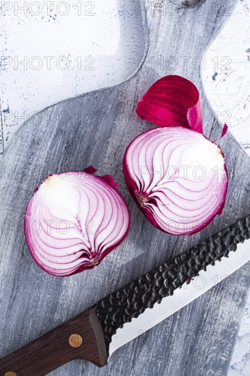 A vibrant red onion is cut in half, on a rustic wooden chopping board beside a sharp knife, ready for cooking