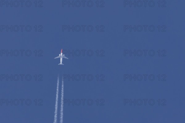 Boeing 737 jet passenger aircraft of Norweign Air with a vapour trial or contrail behind flying in a blue sky, England, United Kingdom