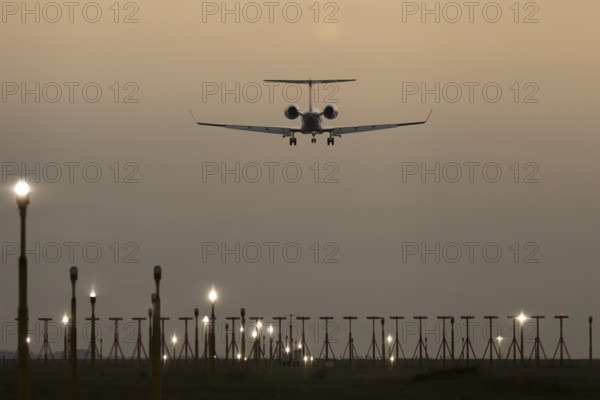 Executive business jet passenger aircraft landing over runway lights at sunset, London Stansted airport, Essex, England, United Kingdom