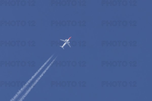 Boeing 737 jet passenger aircraft of Norweign Air with a vapour trial or contrail behind flying in a blue sky, England, United Kingdom