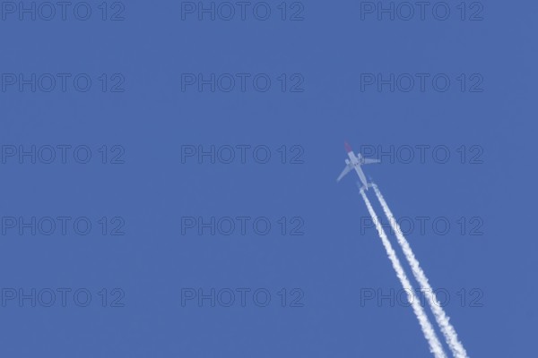 Boeing 737 jet passenger aircraft of Norweign Air with a vapour trial or contrail behind flying in a blue sky, England, United Kingdom