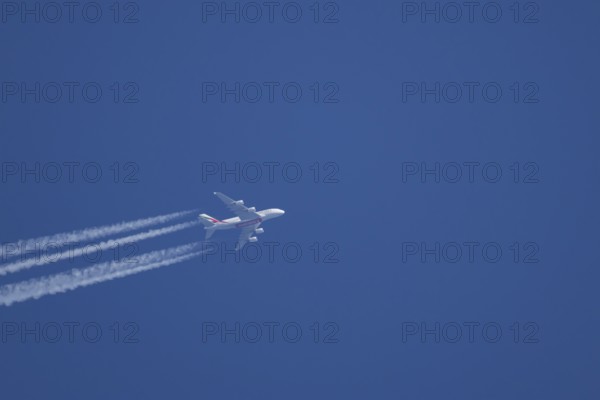 Airbus A380 jet passenger aircraft of Emirates airlines flying with vapour trails or contrails behind in a blue sky, England, United Kingdom