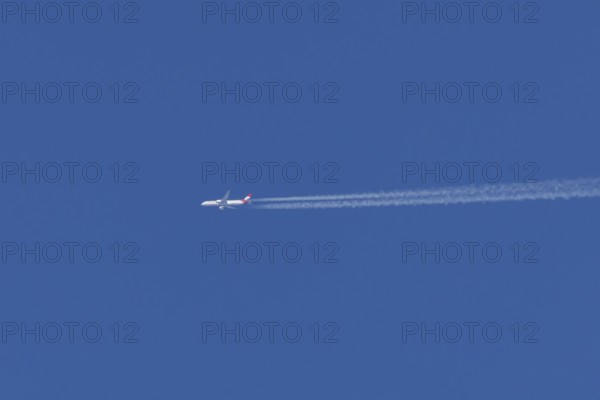 Airbus passenger jet aircraft of Austrian Airlines flying with a vapour trial or contrail behind in a blue sky, England, United Kingdom