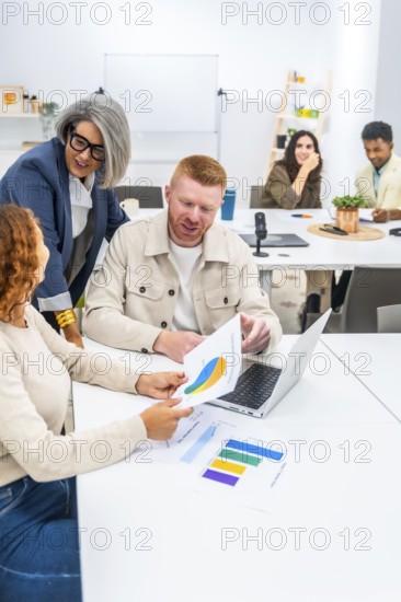 Business professionals collaborating and discussing marketing data with charts and graphs on documents and a laptop during a corporate meeting in a modern office