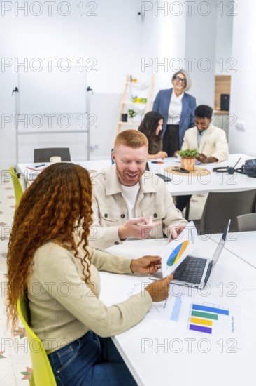 Multicultural business colleagues analyzing financial data and charts on paper and laptop, sharing ideas and discussing project strategies during a collaborative workday in modern office
