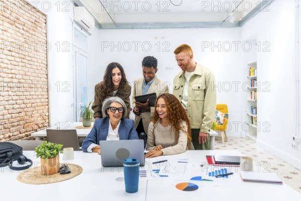 Diverse business team is collaborating and actively discussing financial data shown on a laptop screen, working together in a modern office environment