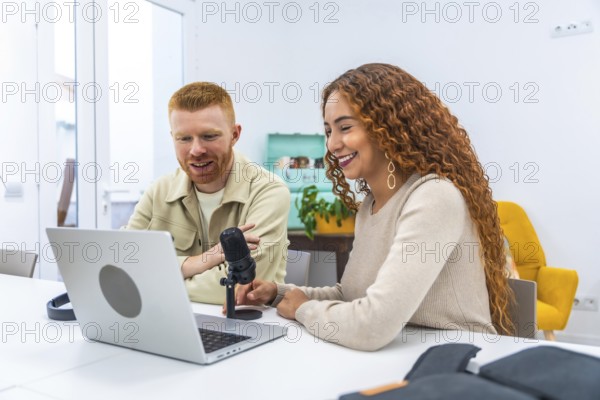 Engaging male and female content creators collaborating on a podcast, recording audio for digital media using a laptop and microphone, sharing ideas and smiling happily