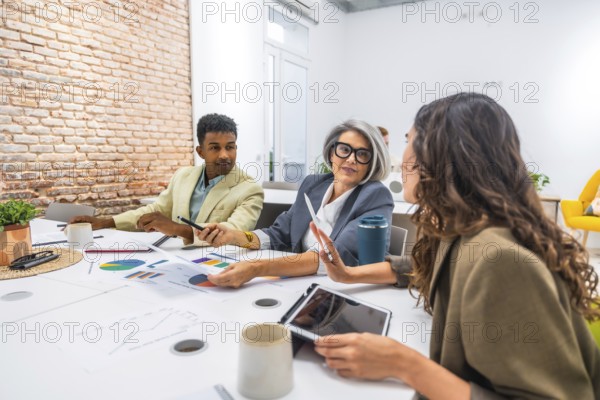 Diverse business professionals collaborating in a modern office. Analyzing data and discussing financial charts during a productive team meeting. Demonstrating teamwork and professional communication