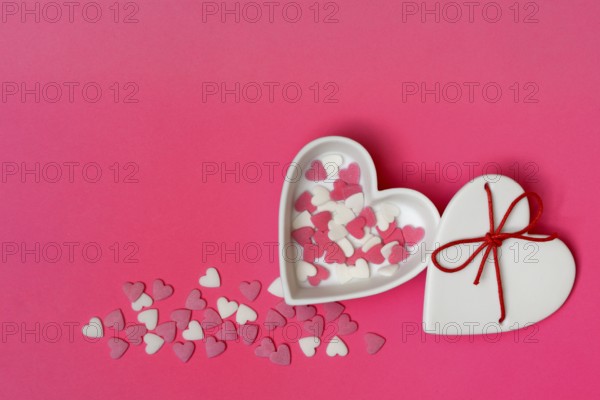 Sugar hearts in a heart-shaped bowl on a pink background