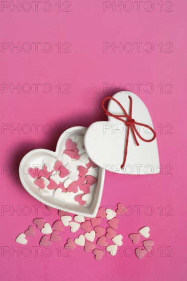 Sugar hearts in a heart-shaped bowl on a pink background