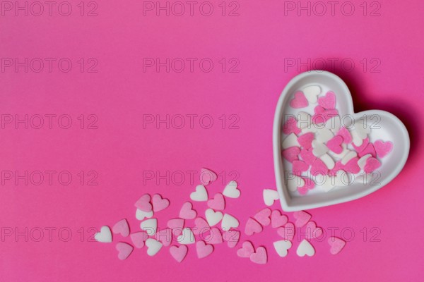 Sugar hearts in a heart-shaped bowl on a pink background