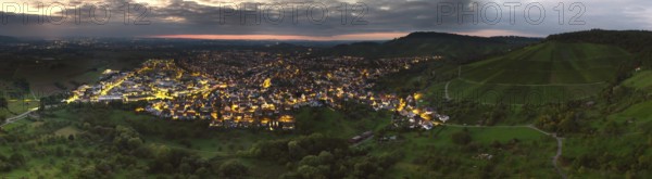 Hilly landscape with illuminated town at sunset under a cloud cover, Korb im Remstal, Baden-Württemberg, Germany