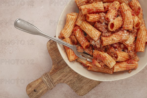 Rigatoni pasta with meat sauce and parmesan cheese on a light table, top view, homemade, no people