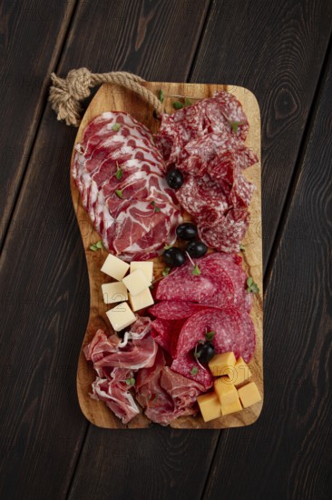 Assorted, sliced meat appetizer, prosciutto, salami and ham, with cheese and olives, on a wooden board, breakfast, top view, close-up, no people
