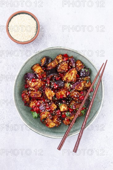 Fried eggplant, Chinese style, in sweet and sour sauce, with pepper and sesame seeds, in a green bowl