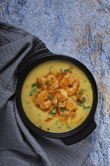Creamy shrimp curry with spices, garnished with herbs, on a textured background, homemade, no people
