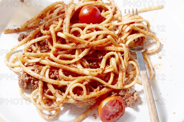 A plate holds freshly cooked spaghetti topped with flavorful meat sauce and garnished with bright cherry tomatoes. A glass sits nearby, reflecting a relaxed dining atmosphere