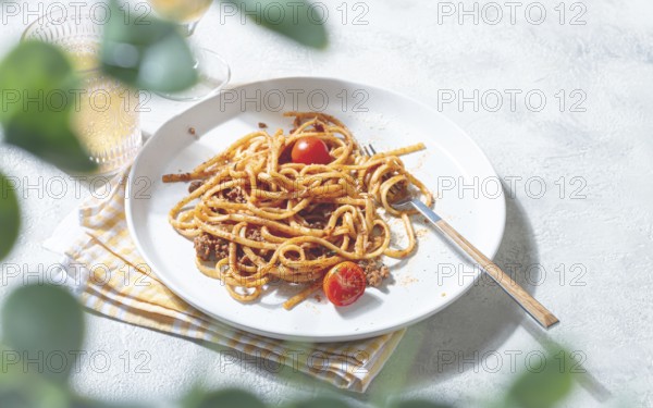 A plate of perfectly cooked spaghetti is topped with rich sauce and fresh tomatoes. Next to it, a glass of cold drink sits on a light tablecloth, creating a cozy dining scene