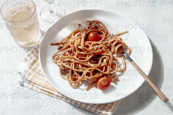 Freshly cooked spaghetti topped with savory meat sauce and garnished with cherry tomatoes is elegantly presented on a white plate alongside a glass of wine