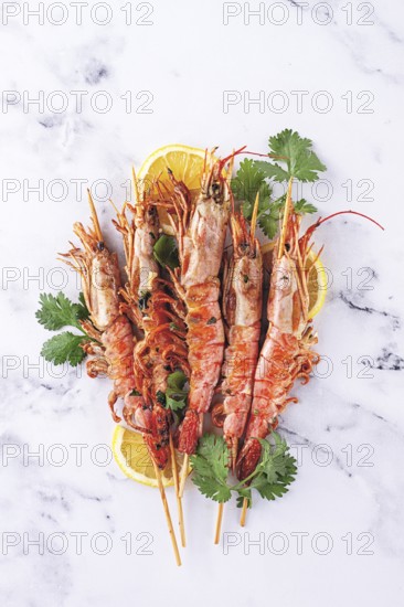 Shrimps on skewers, Grilled, spread on a marble surface, garnished with lemon slices and fresh herbs. view from above