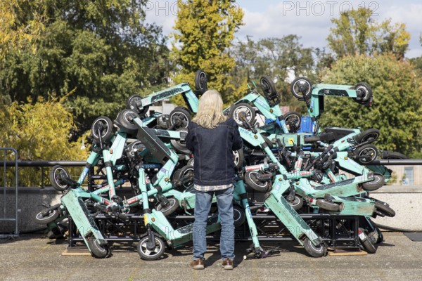 A man looks at an exhibit with stacked e-scooters on the roof terrace of the Haus der Kulturen der Welt at the HKW Takeover: The Possibility of Unreason by Jan Böhmermann & Gruppe Royale. The exhibition will be accompanied by concerts, shows, TV recordings, performances, film screenings and talks from 27 September to 19 October 2025