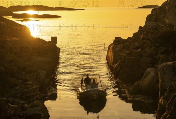 Motorboat with two persons sailing in harbour entrance at sunset, archipelago, Smögen, Smögenbryggan, Västra Götalands Län, Bohuslän, Sweden