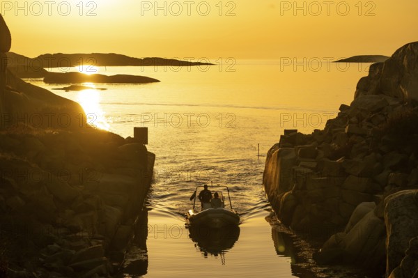 Motorboat with two persons sailing in harbour entrance at sunset, archipelago, Smögen, Smögenbryggan, Västra Götalands Län, Bohuslän, Sweden